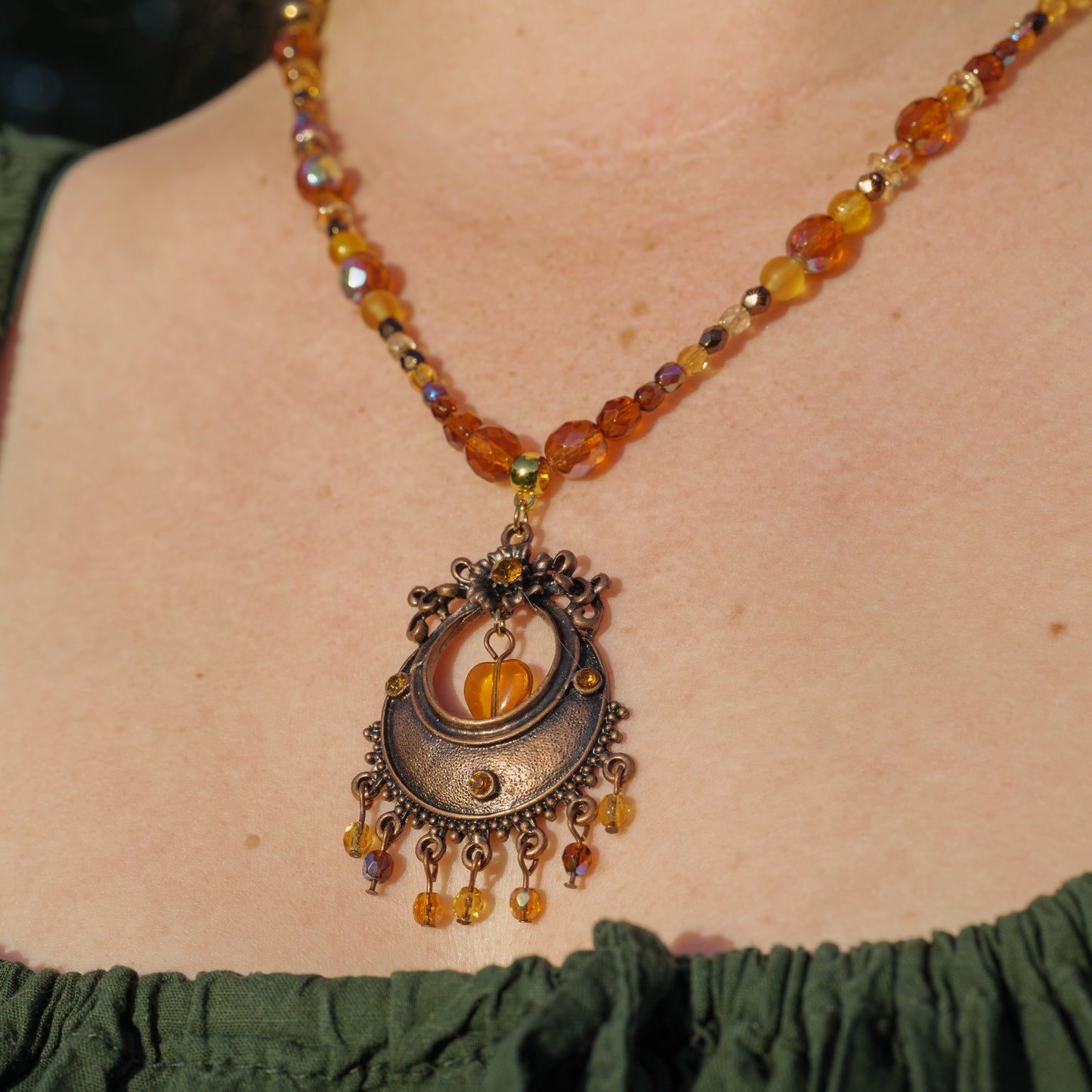 Ketting met antiek koperkleurig rond ornament met hart en amberkleurige facetkralen