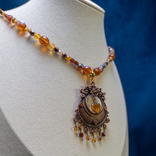 Ketting met antiek koperkleurig rond ornament met hart en amberkleurige facetkralen