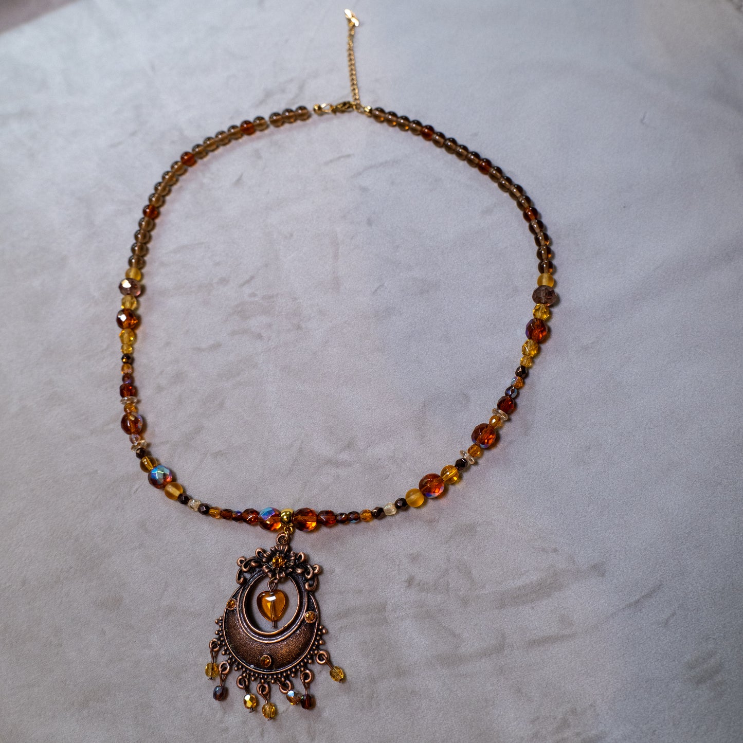 Ketting met antiek koperkleurig rond ornament met hart en amberkleurige facetkralen