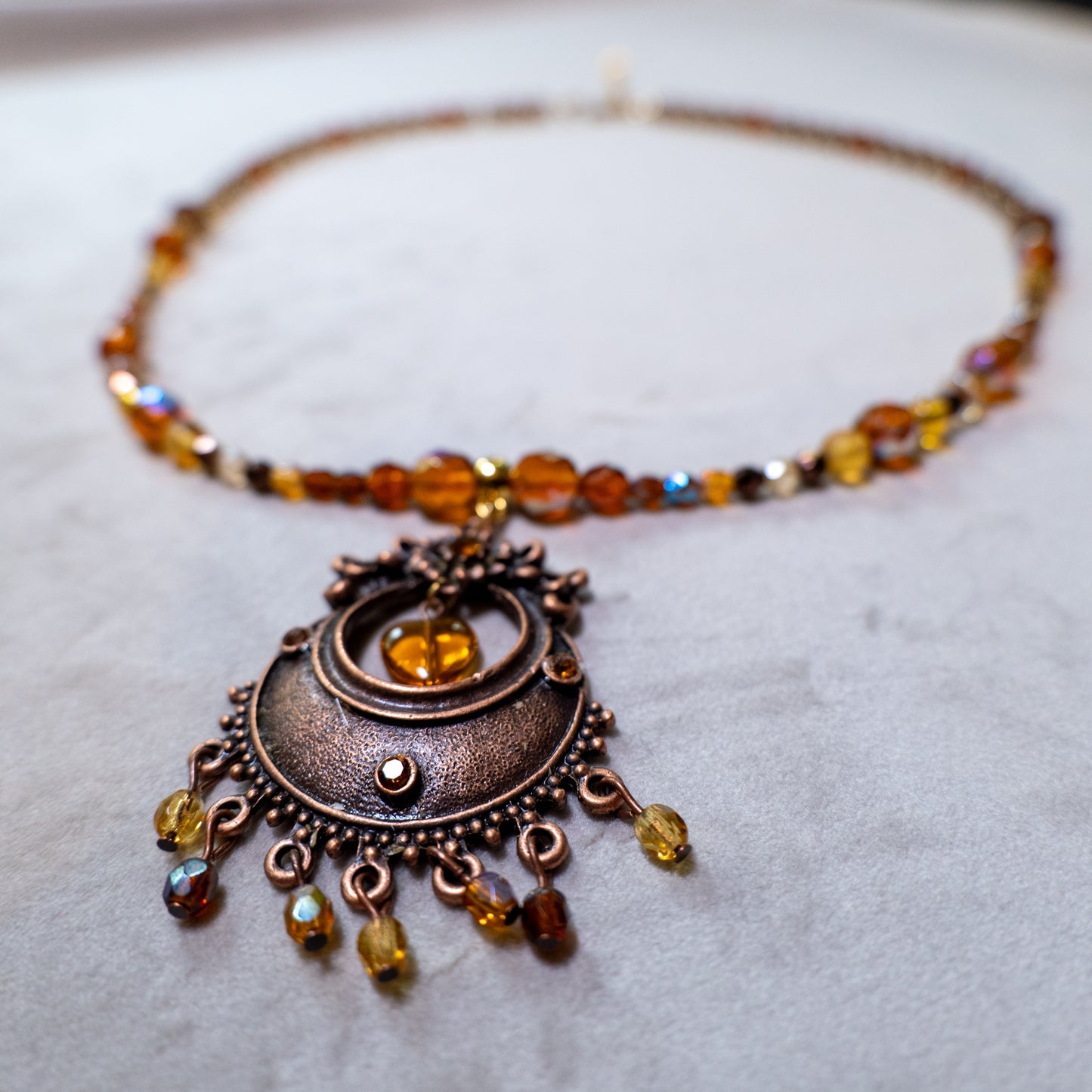 Ketting met antiek koperkleurig rond ornament met hart en amberkleurige facetkralen