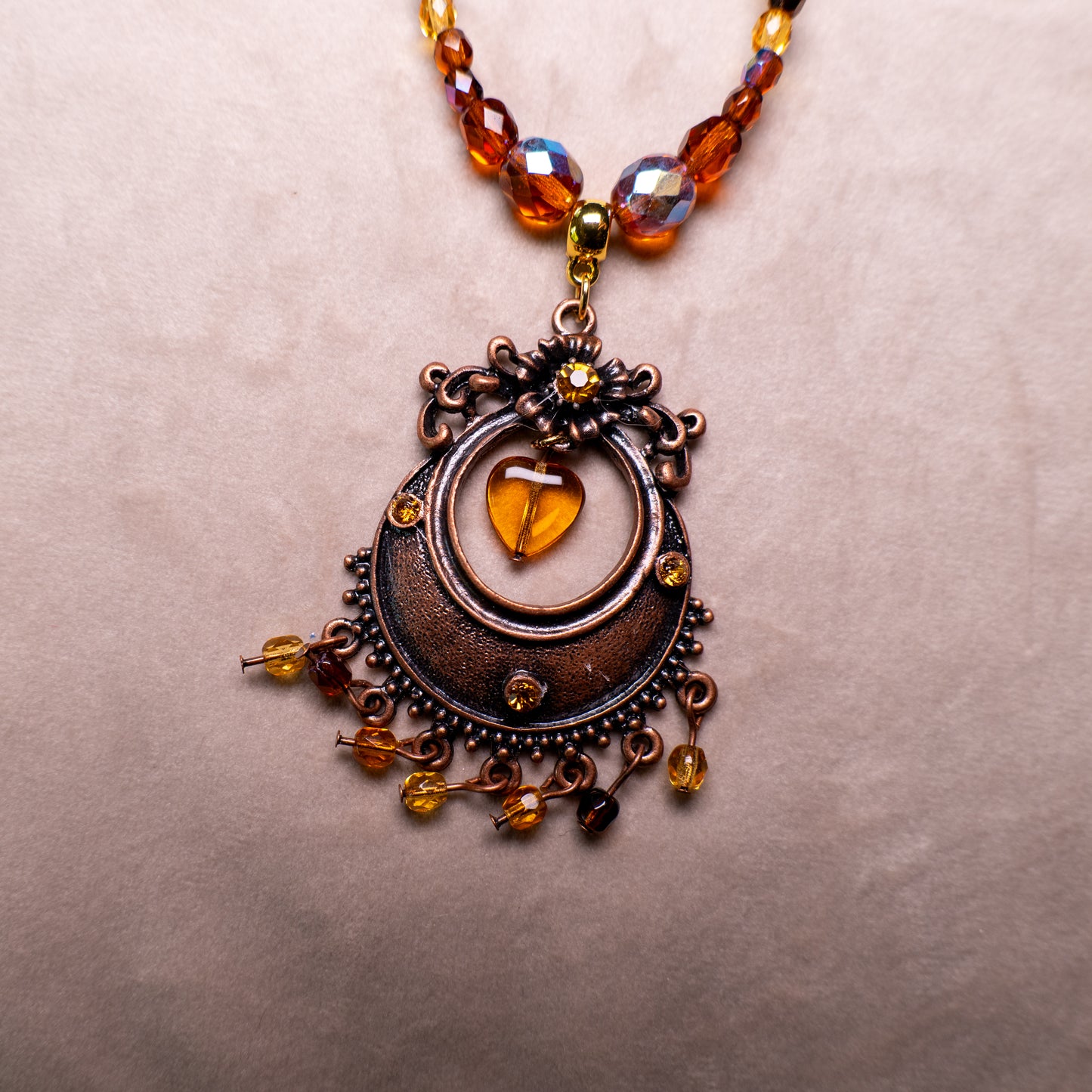 Ketting met antiek koperkleurig rond ornament met hart en amberkleurige facetkralen