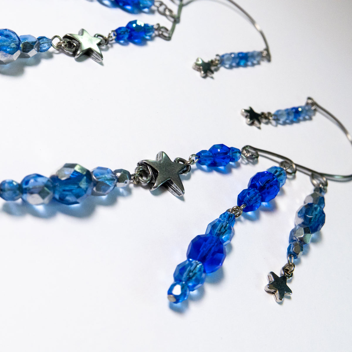 Ear cuffs vallende sterren op een witte achtergrond. Ear cuffs met blauwe facetglaskralen en diverse metalen sterren. Detailfoto blauwe kralen.