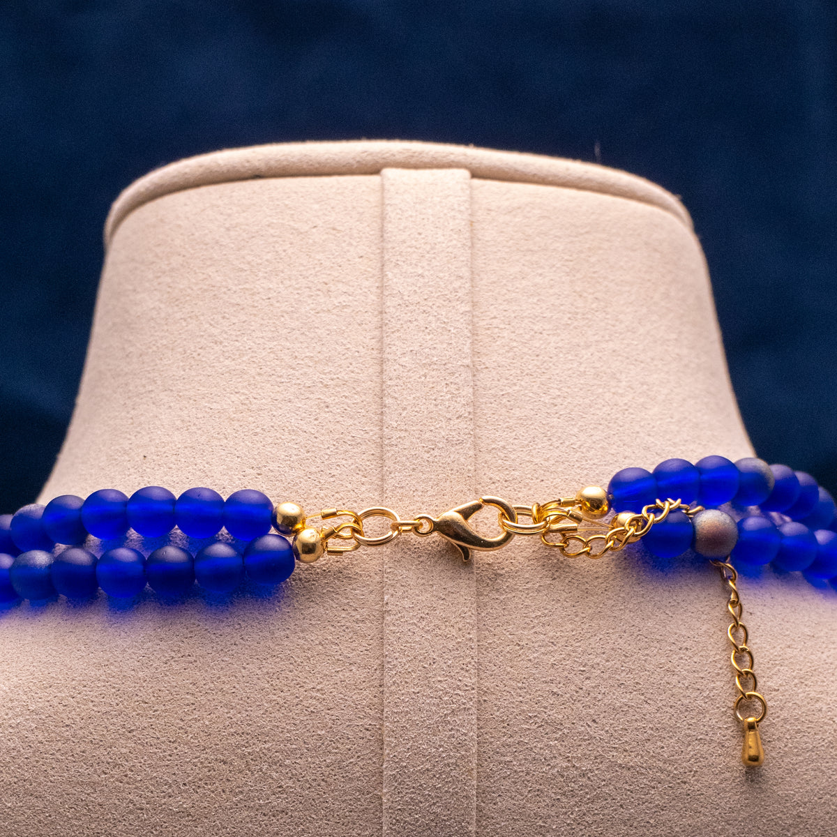 Ketting wandering stars op een beige buste. Met blauwe en gele kralen en goudkleurige accenten. Detailfoto sluiting
