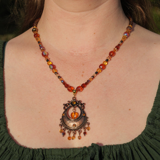 Ketting met antiek koperkleurig rond ornament met hart en amberkleurige facetkralen