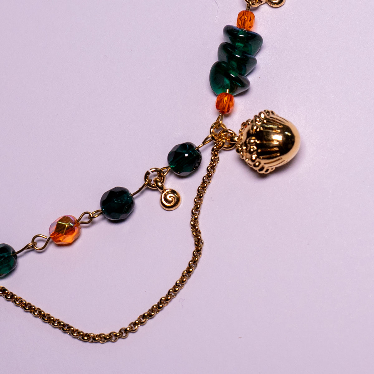 De ketting Oakheart op een witte achtergond Oranje en groene glaskralen gecombineerd met goudkleurige hangende elementen en basismaterialen. Detailfoto van eikel.