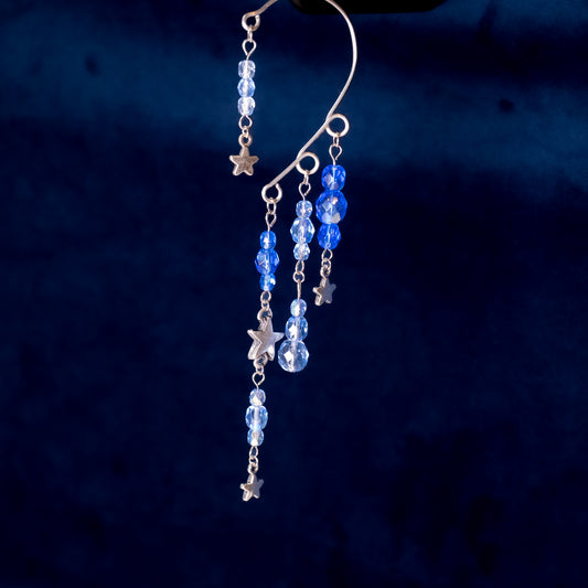 Ear cuffs vallende sterren mini op een blauwe achtergrond. Blauwe facetglaskralen met zilverkleurige metalen sterren.