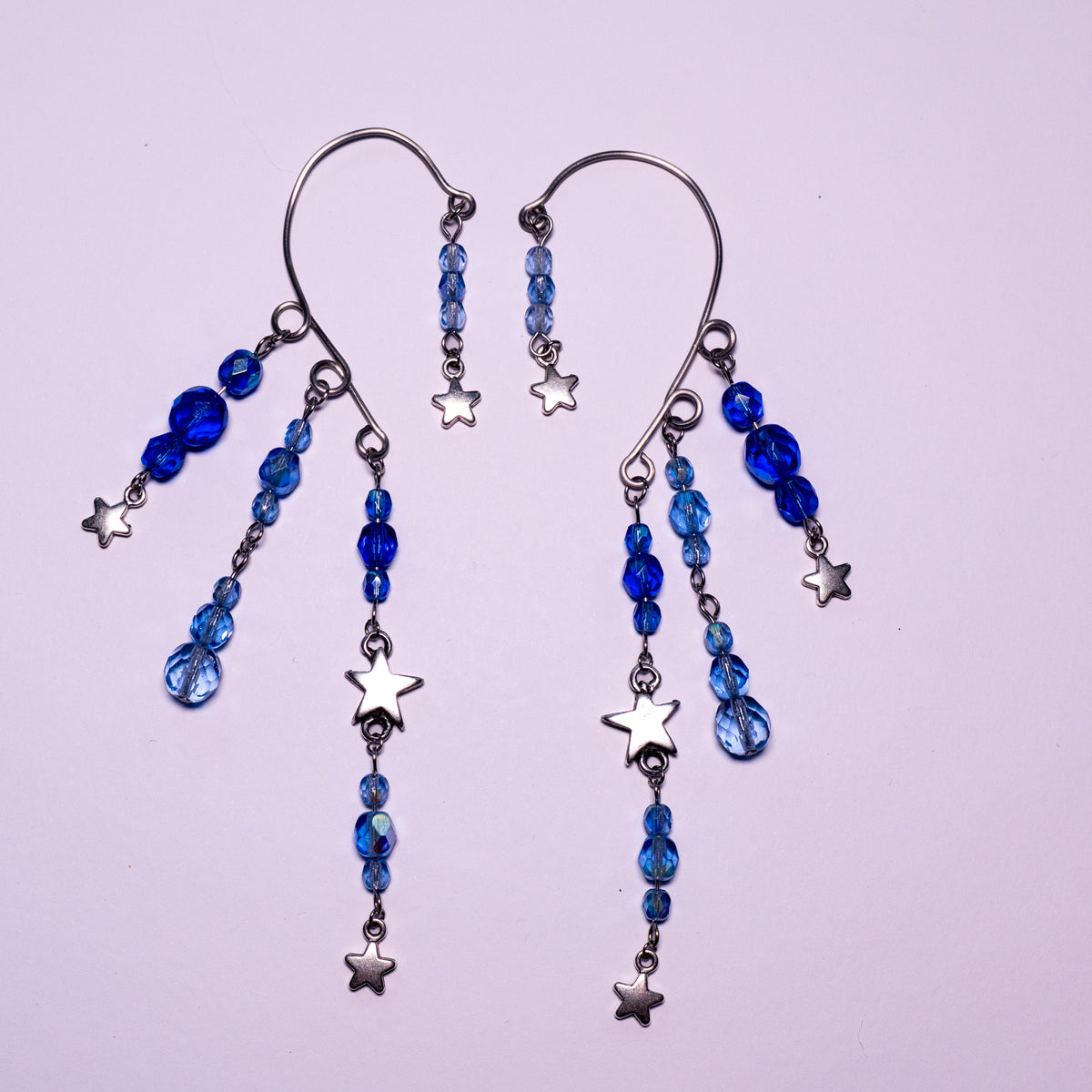 Ear cuffs vallende sterren mini op een witte achtergrond. Blauwe facetglaskralen met zilverkleurige metalen sterren.