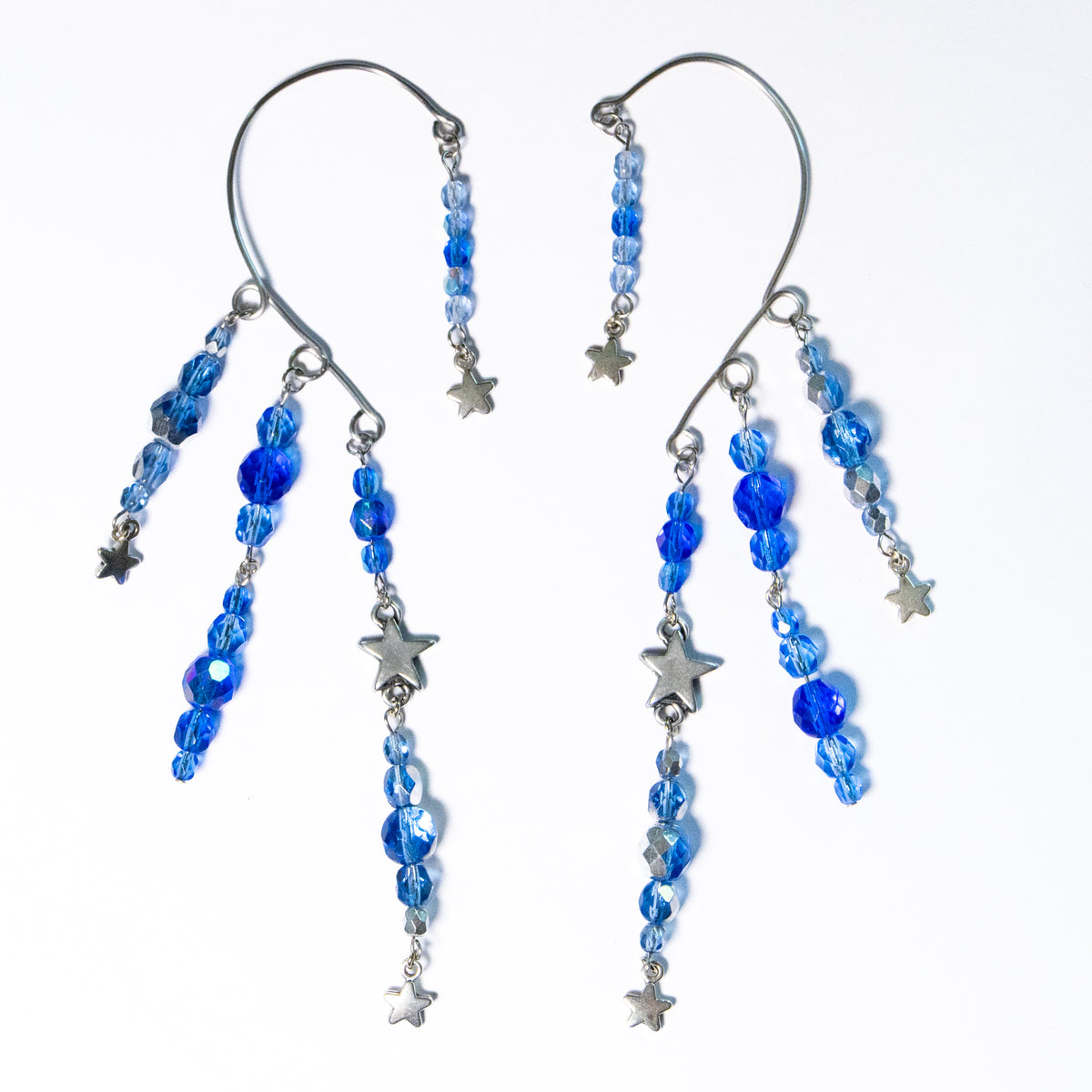 Ear cuffs vallende sterren op een witte achtergrond. Ear cuffs met blauwe facetglaskralen en diverse metalen sterren.