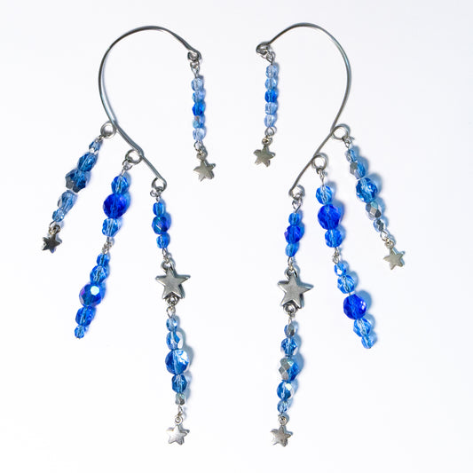 Ear cuffs vallende sterren op een witte achtergrond. Ear cuffs met blauwe facetglaskralen en diverse metalen sterren.