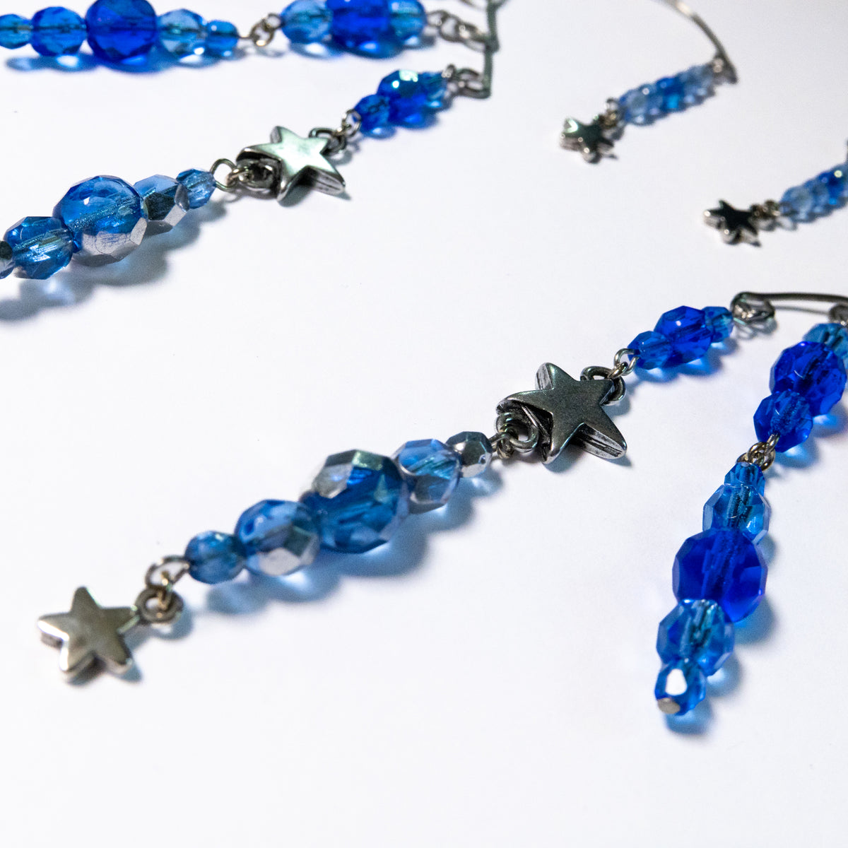 Ear cuffs vallende sterren op een witte achtergrond. Ear cuffs met blauwe facetglaskralen en diverse metalen sterren. Detailfoto grote ster.