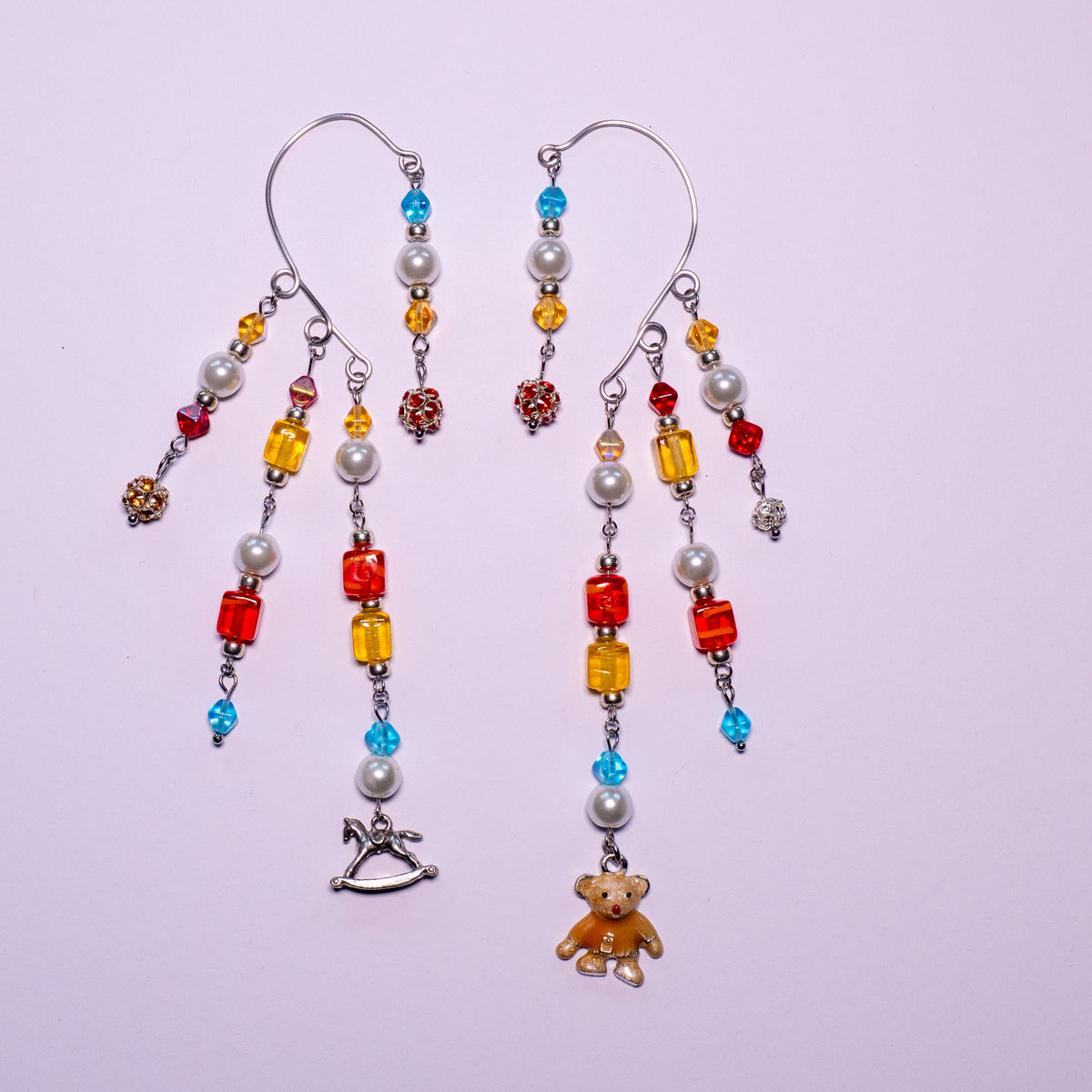 Speelgoedkist ear cuffs op een witte achtergrond. Bevat strassballetjes in drie kleuren: rood, geel en wit; vierkante kralen in geel en rood; pyramidekralen in geel, blauw en rood; witte glasparels; en een bedel van een hobbelpaard en een beertje.