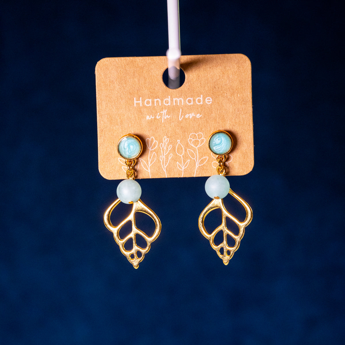 Sunlit Shell oorbellen met matte turquoise kralen en opengewerkte goudkleurige schelphangers aan een kartonnen sieradenkaart met de tekst 'Handmade with Love'.