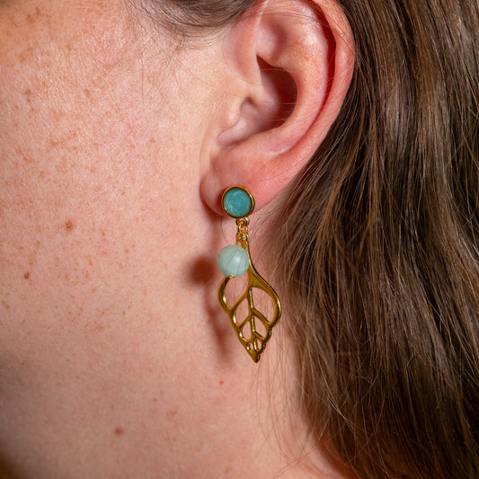 Sunlit Shell oorbel met matte turquoise kralen en opengewerkte goudkleurige schelphangers aan een oor.